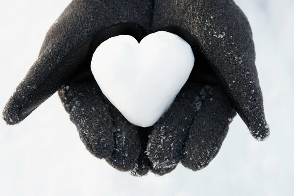 A white heart made of snow in the palms of your hands