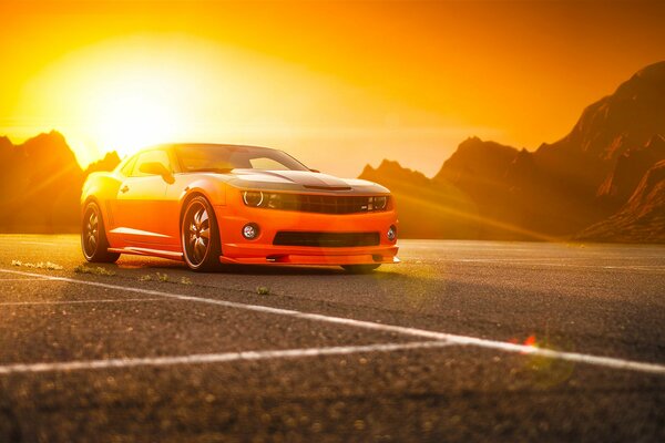 Orange SS Camaro on the background of mountains and the sun