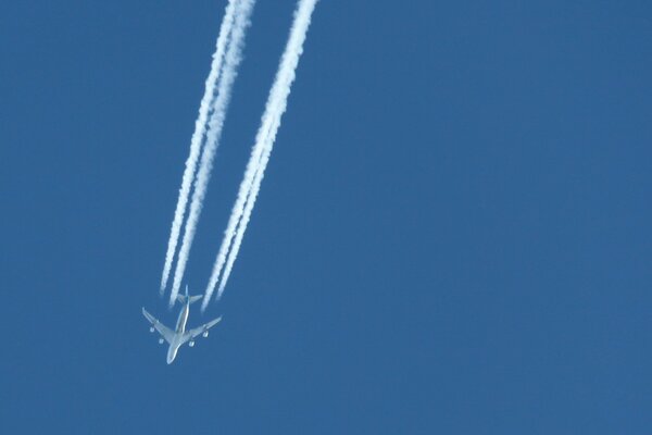 The plane flies in the blue sky leaving a white trail