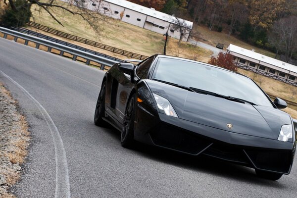 A black Lamborghini rides on a road with bumpers on the edges against the background of an autumn rustic landscape