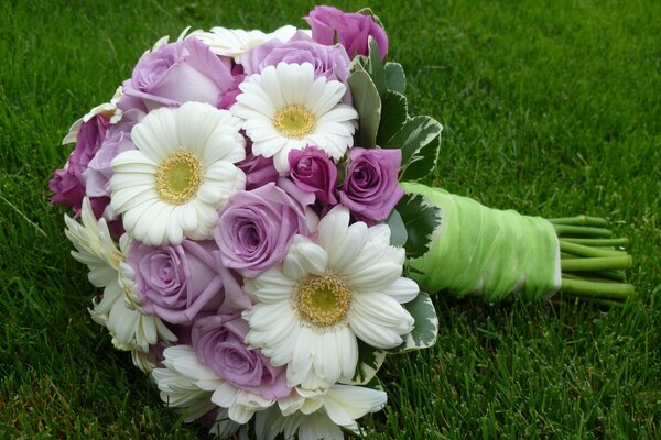 A bouquet of chamomile and roses lies on the grass