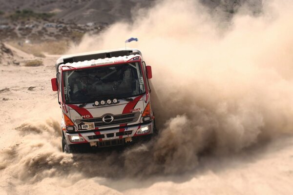 A sports truck is dusting on the highway on the sand