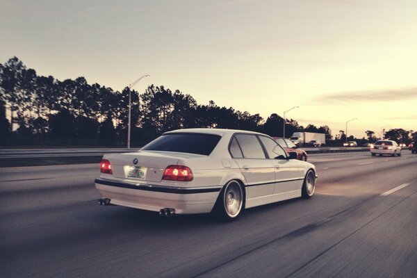White BMW e38 rushes at speed on the highway