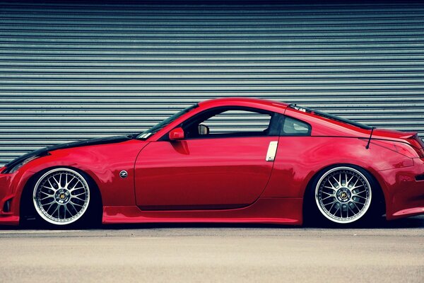 Photo of a red nissan 350z on the background of a closed roller shutter