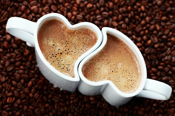 Two coffee mugs with a heart shape on the background of coffee beans