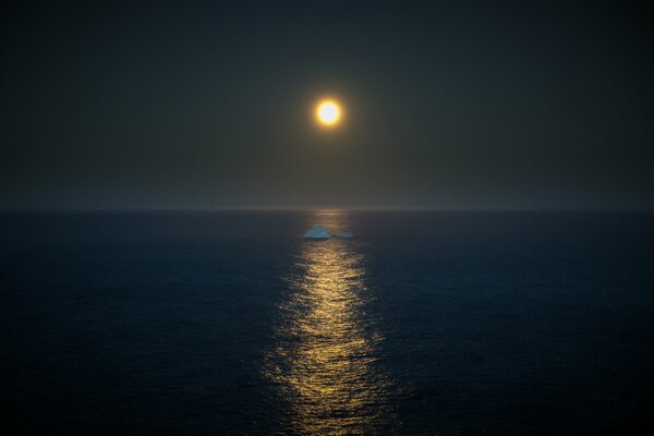 An iceberg floats in the middle of the sea in the light of the full moon