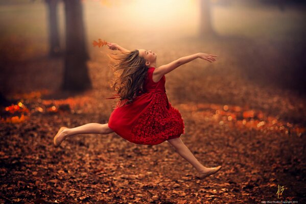 A girl runs in a red dress through the leaves