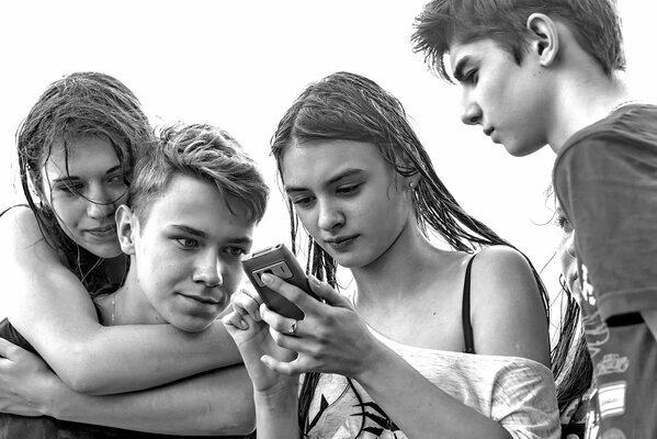 Two guys and two girls soaked through are enthusiastically looking at the phone