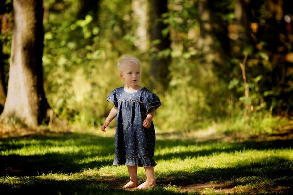 A baby in a dress in a forest clearing