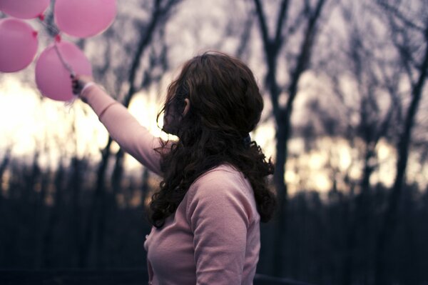 The girl is holding pink balloons with a blurry background behind her