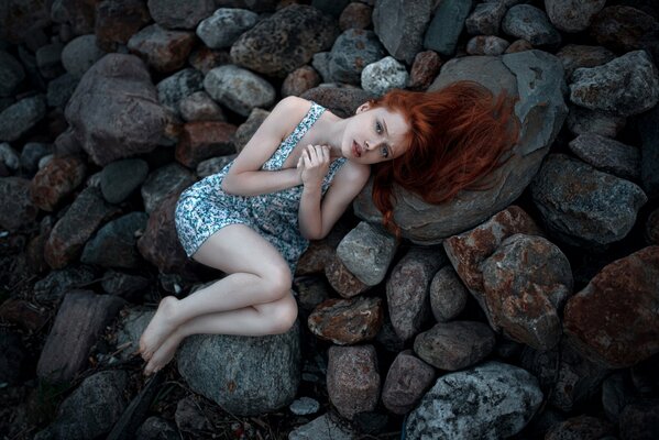 A red-haired girl with freckles is lying on a cold stone