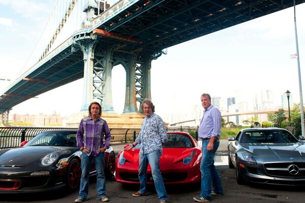 Three sports cars and three men are standing under the bridge