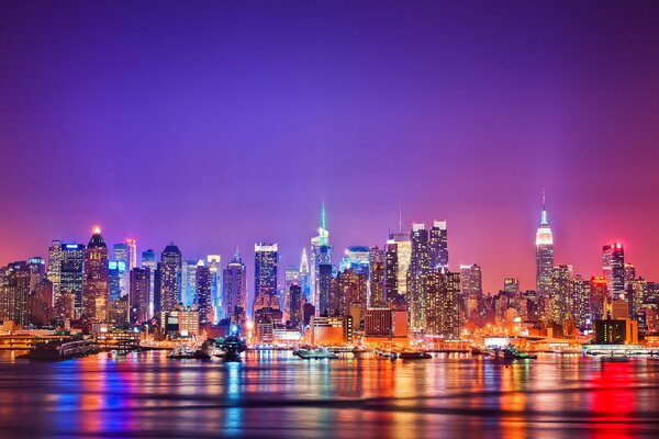 The lights of Manhattan at night are reflected in the Hudson River