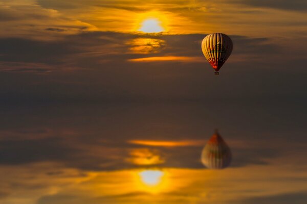 Reflection in the water of a balloon flying at sunset