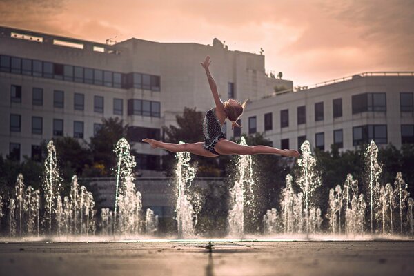 A girl in flight does the splits against the background of fountains and buildings