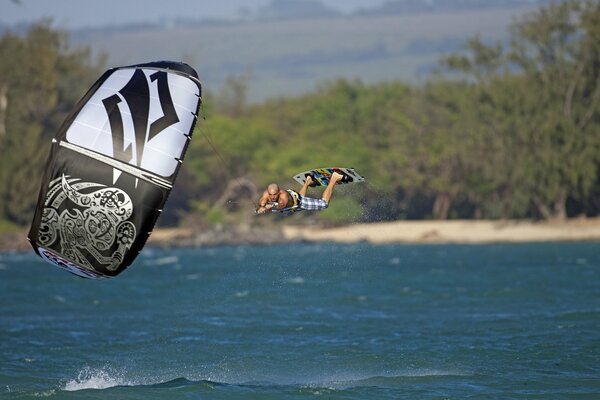 Surfer flies over the sea, holding on to a parachute