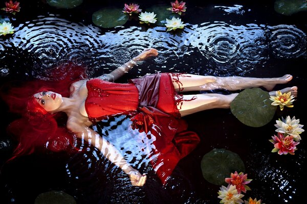 A girl with red hair lies in the water with water lilies