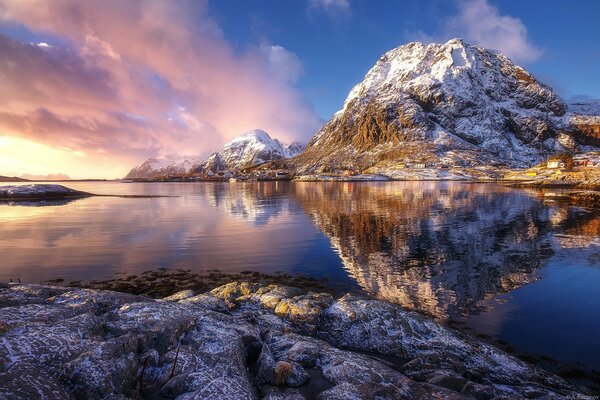 Pink sunset and snowy rocks are reflected in the blue water