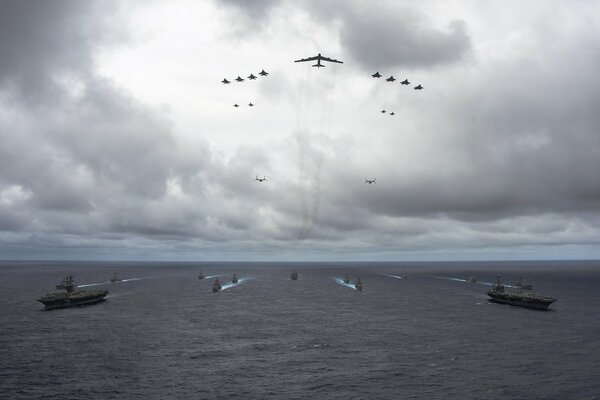 A flock of planes flies over warships