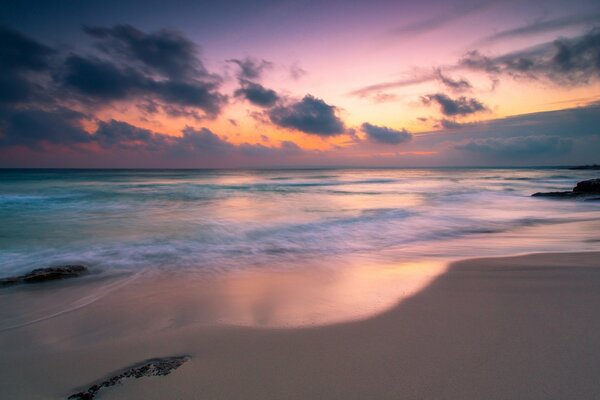 The pink sky is reflected in the waters of the calm sea