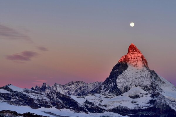 The top of the Alps against the twilight sky. Moon over the top