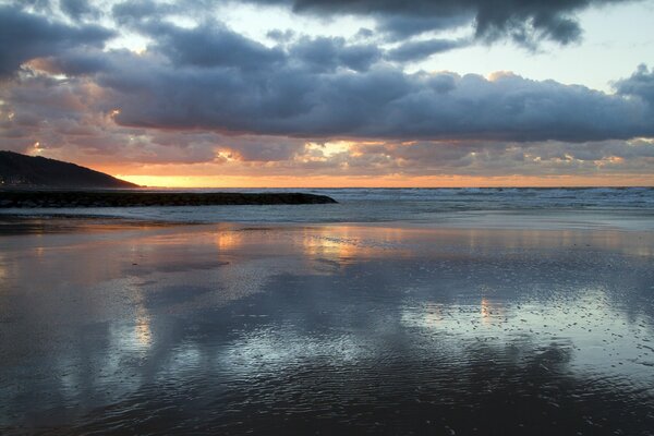 The sunset can be seen from the horizon, the sea wave is beating against the pier